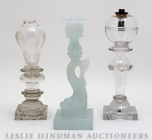 A Collection of American Glass Lighting Articles, : A Collection of American Glass Lighting Articles, 19th century, comprising a sandwich glass fluid lamp, a cut glass fluid lamp and a dolphin form candlestick. Height of tallest 10 7/8 inches. Property