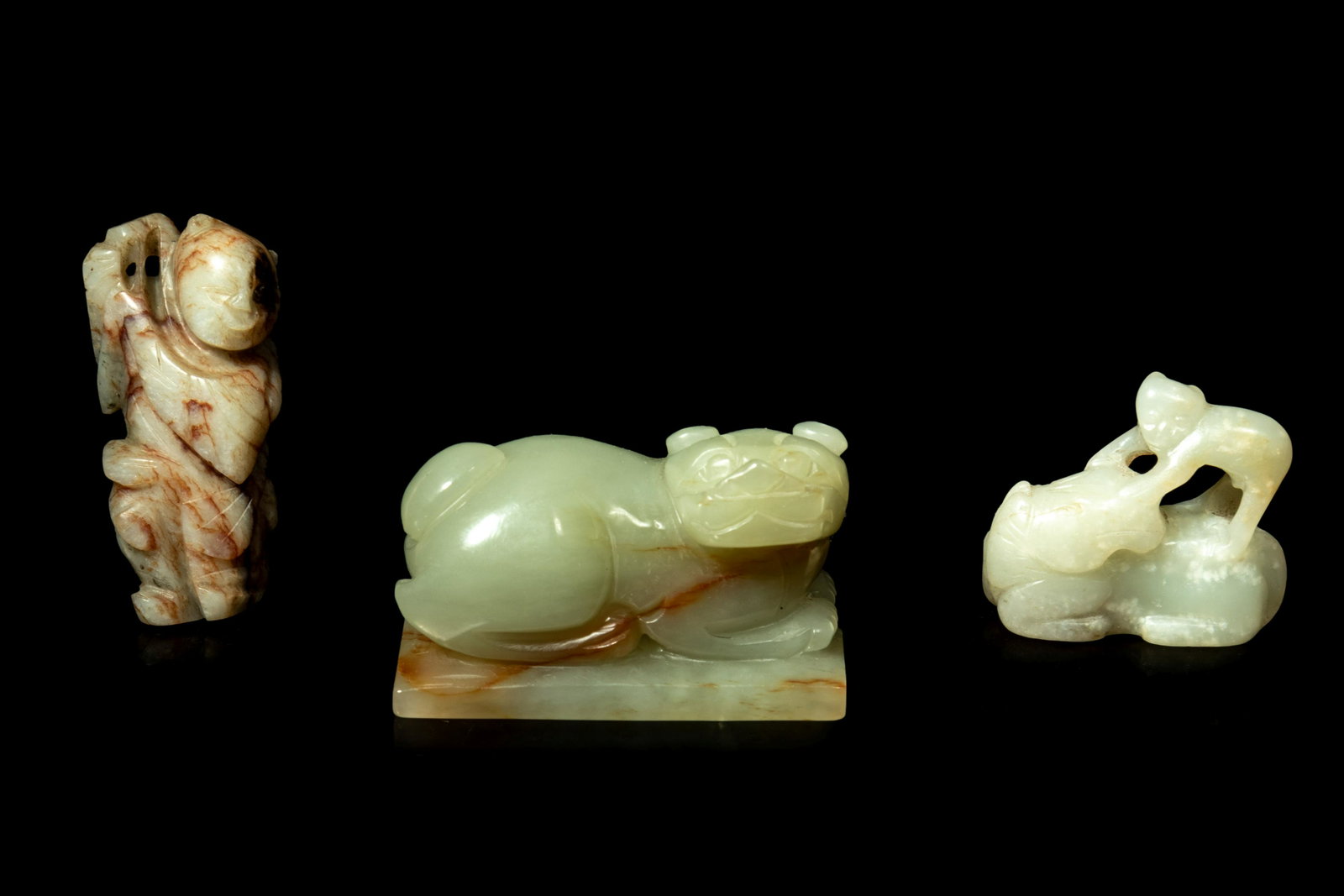 Three Chinese Jade Carvings: Three Chinese Jade Carvings comprising a celadon and russet figure of a dog, a celadon horse and monkey group, and a chicken bone figure of a boy. Length of largest 2 3/8 in., 6 cm.