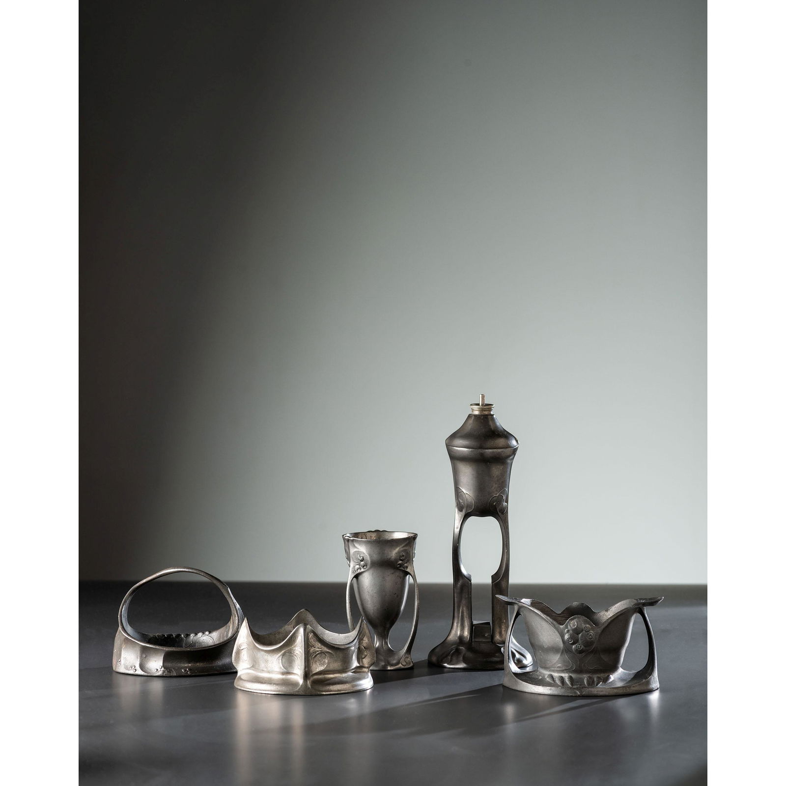 Five Kayserzinn Jugendstil Pewter Wares: Five Kayserzinn Jugendstil Pewter Wares German, Early 20th Century comprising an oil lamp, two wine coasters, a vase and a handled dish, model numbers 4489, 4535, 4435, 4512 and 4476; all marked. Heig