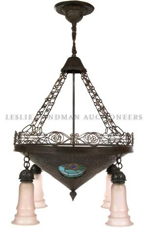 An Art Deco Eight-Light Fixture, Diameter 28 inch: An Art Deco Eight-Light Fixture, the standard issuing four lights above a conical hammered metal shade inset with four leaded glass panels, the frame having scrolling and geometric decoration and issu