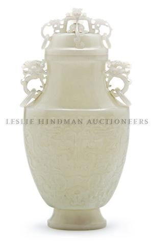 A White Jade Vase and Cover, Height 10 inches.: A White Jade Vase and Cover, of flattened ovoid form having lion form finial above the lion mask and loose ring handles, the main body of spade form with raised taotie style decoration, raised upon a