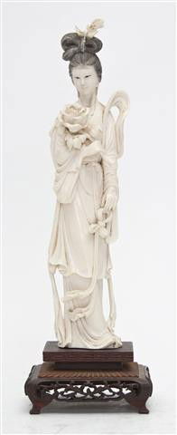 A Chinese Carved Ivory Figure of a Lady, Height 10: A Chinese Carved Ivory Figure of a Lady, depicted holding a blossom, having flowing robes, raised on a rectangular carved wood base ending in four bracket feet. Height 10 inches.