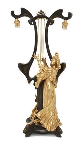 A Gilt and Patinated Bronze Figural Lamp, Pfeffer: A Gilt and Patinated Bronze Figural Lamp, Pfeffer, cast as an Art Nouveau maiden playing a lyre from which the two lighting elements hang. Height 20 inches.