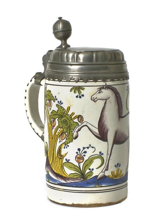 A Continental Pewter Mounted Faience Tankard, Height 10: A Continental Pewter Mounted Faience Tankard, 18th century, of cylindrical form, having a white horse and polychrome foliate decoration. Height 10 inches.