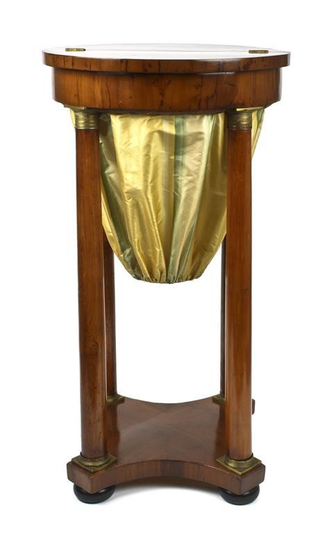 A Biedermeier Sewing Table, Height 33 1/4 inches.: A Biedermeier Sewing Table, the top of circular form with hinged lid, raised on four columns with gilt metal mounts, joined by a shaped medial shelf, raised on ebonized wood bun feet. Height 33 1/4 in