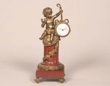 A Louis XV Style Gilt Metal and Marble F: A Louis XV Style Gilt Metal and Marble Figural Clock, modeled as a putto sitting on a marble column holding the clock by a ribbon, the clock with an enamel dial, the column decorated with floral swag.
