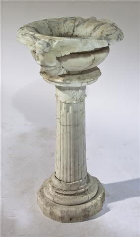 An Alabaster Bird Bath, Height 42 1/2 inches.: An Alabaster Bird Bath, the circular bowl with angel and mask decoration, raised on a reeded column over a stepped base. Height 42 1/2 inches.