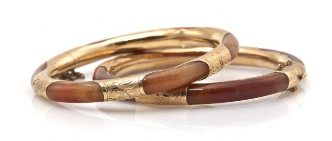 A Pair of 14 Karat Yellow Gold and Jade Bangle Bra: A Pair of 14 Karat Yellow Gold and Jade Bangle Bracelets, consisting of orange-brown jade partially enclosed within engraved gold settings. Stamp: 14K 585. 34.80 dwts.