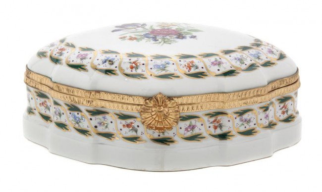 A Limoges Porcelain and Gilt Metal Mounted Box, Wi: A Limoges Porcelain and Gilt Metal Mounted Box, 20th century, of shaped oval form, the hinged lid centered with a spray of flowers within a repeating floral and gilt border. Width 11 inches.