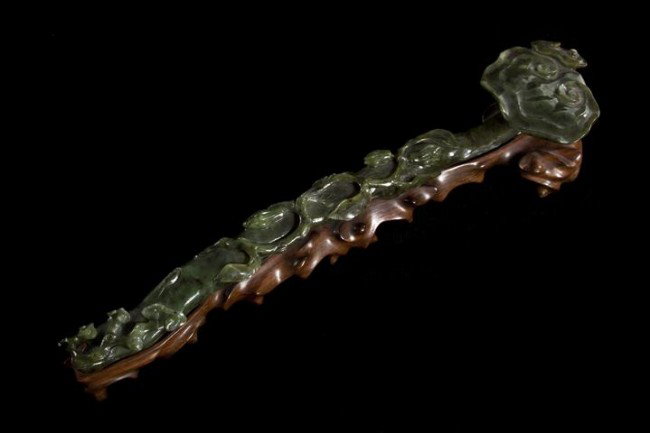 A Spinach Jade Ruyi Scepter, Length 14 inches.: A Spinach Jade Ruyi Scepter, having linghzi fungus form head with naturalistically craggy form handle, raised atop a fitted wood base. Length 14 inches. Property of a Private Collector, Chicago, Illin