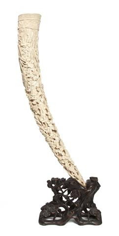 A Carved Ivory Tusk, Length of ivory 18 1/2 inches: A Carved Ivory Tusk, deeply carved throughout showing figures in a landscape at various tasks, raised upon a fitted and pierce carved wood base. Length of ivory 18 1/2 inches. Property of a Private Co