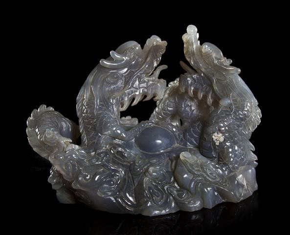 A Chinese Carved Chalcedony Model of Dragons, Widt: A Chinese Carved Chalcedony Model of Dragons, the beasts depicted each with a claw clutching a sphere at center raised above rock work carving and swirling waves. Width 8 1/4 x length 5 1/4 inches. Pr