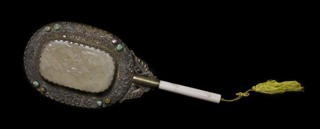 A Jade Inset Silver Hand Mirror, Length 11 1/2 inc: A Jade Inset Silver Hand Mirror, having white jade oval plaque at center with relief carving of a wandering scholar in a landscape surrounded by a band of silver repousse decoration of floral themes w