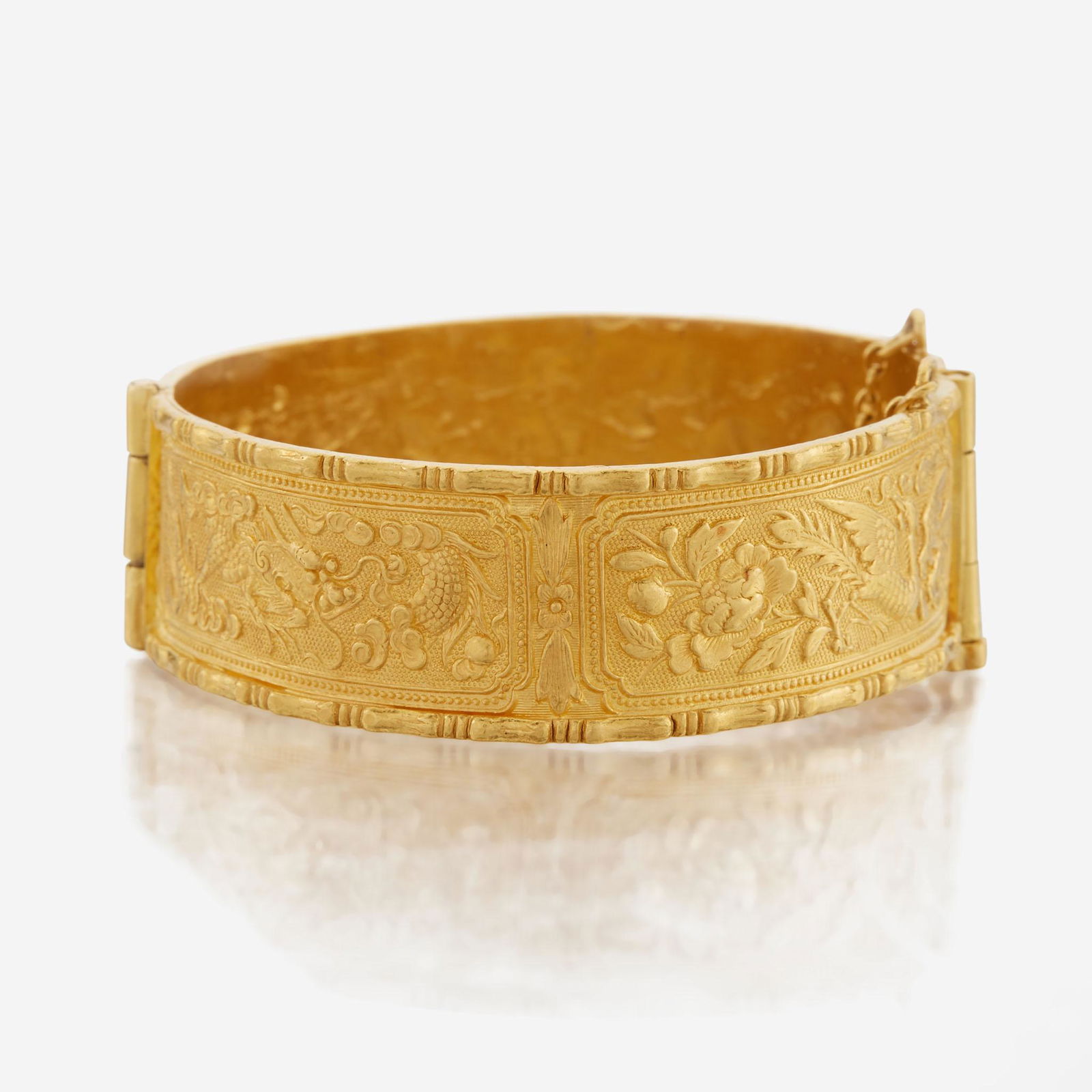 A gold bangle bracelet: A gold bangle bracelet the hinged design with textured and polished 24K gold reliefs of flora and fauna. (33.5 dwt.; Interior circumference: 6 1/2 in.) Please note that the all information provided su