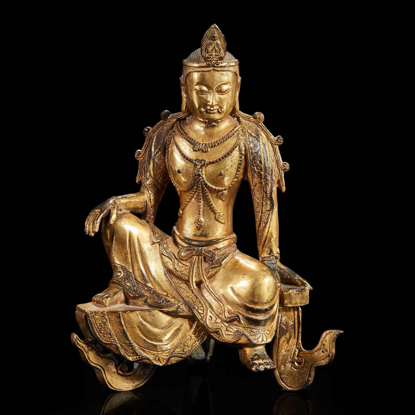 A gilt-bronze figure of a "water-moon" Avalokitesvara: Depicted in male manifestation, with inscribed floral patterns along the border of his robes, seated on a triangular base. (H: 9 3/4 in.)