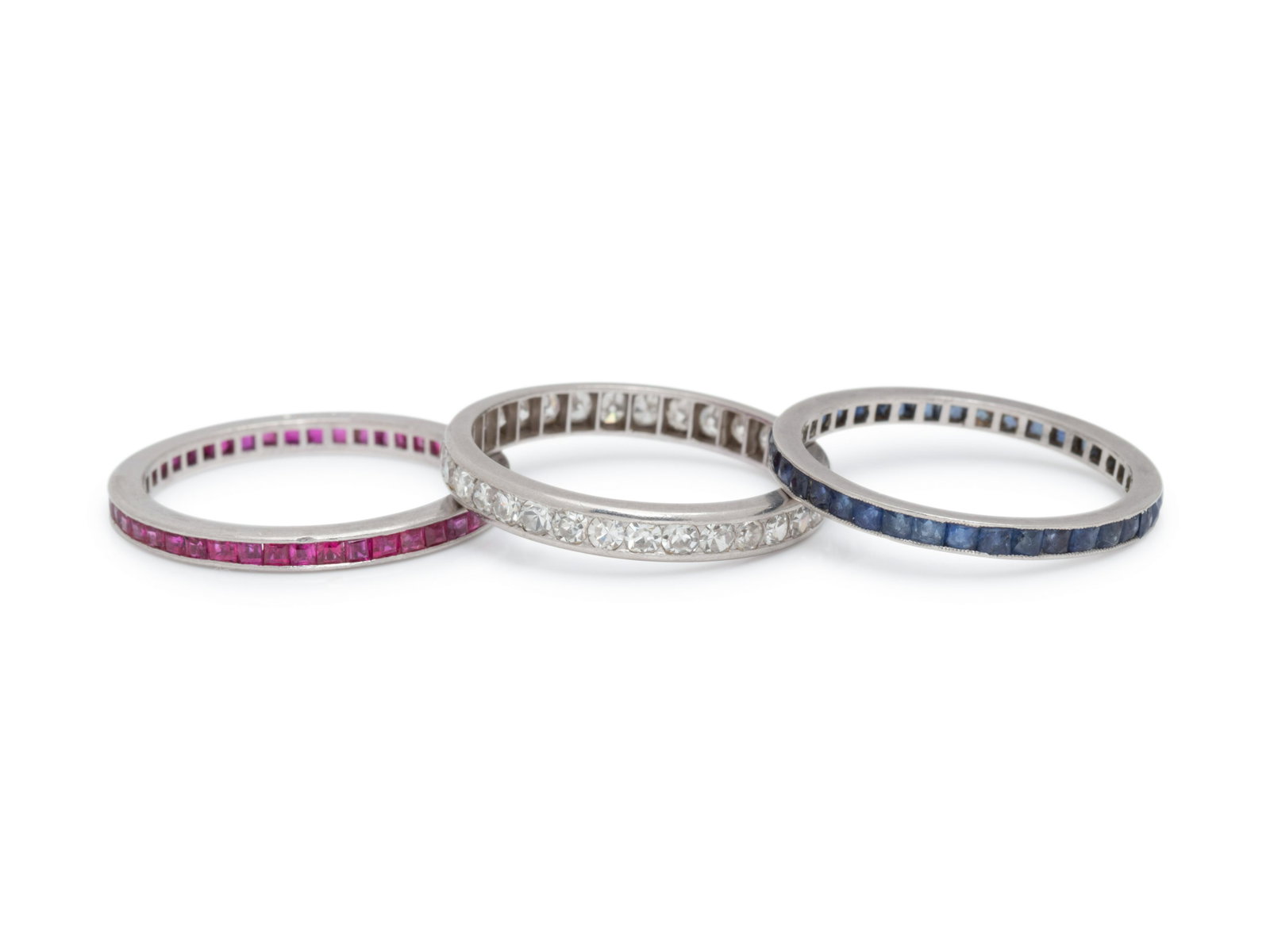 COLLECTION OF ETERNITY BANDS: COLLECTION OF ETERNITY BANDS Consisting of a ring by Cartier containing numerous square step cut rubies, a ring containing numerous French cut sapphires, together with a ring containing numerous singl
