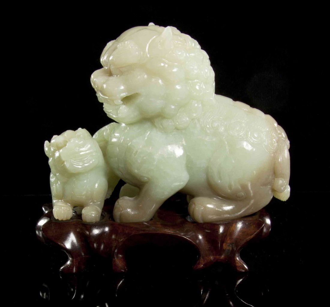A Jade Carving of a Fu Dog and Pup, Width 6 inches: A Jade Carving of a Fu Dog and Pup, depicting the larger animal seated on its haunches with the smaller animal recumbent before it, of light green colored stone with brown tone towards the bottom and