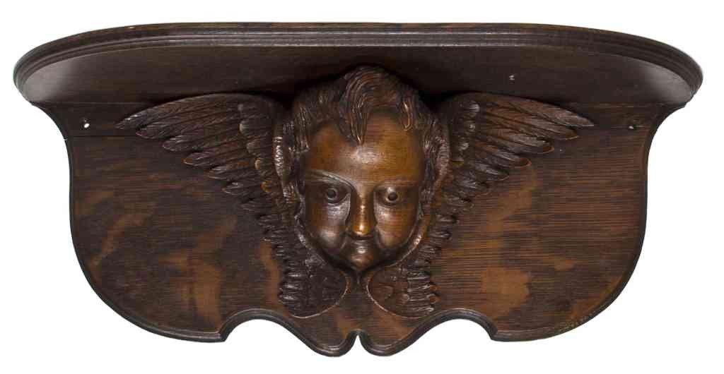 An American Oak Carved Wall Bracket, Width 20 inc: An American Oak Carved Wall Bracket, having a D-shaped top over the cherub mask support. Width 20 inches.