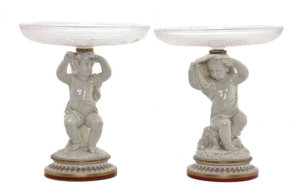 A Pair of English Porcelain and Glass Figural Dis: A Pair of English Porcelain and Glass Figural Dishes, Worcester, the circular molded dishes raised on putti form supports. Height overall 10 1/4 inches. From the Collection of William Kentor of Highla