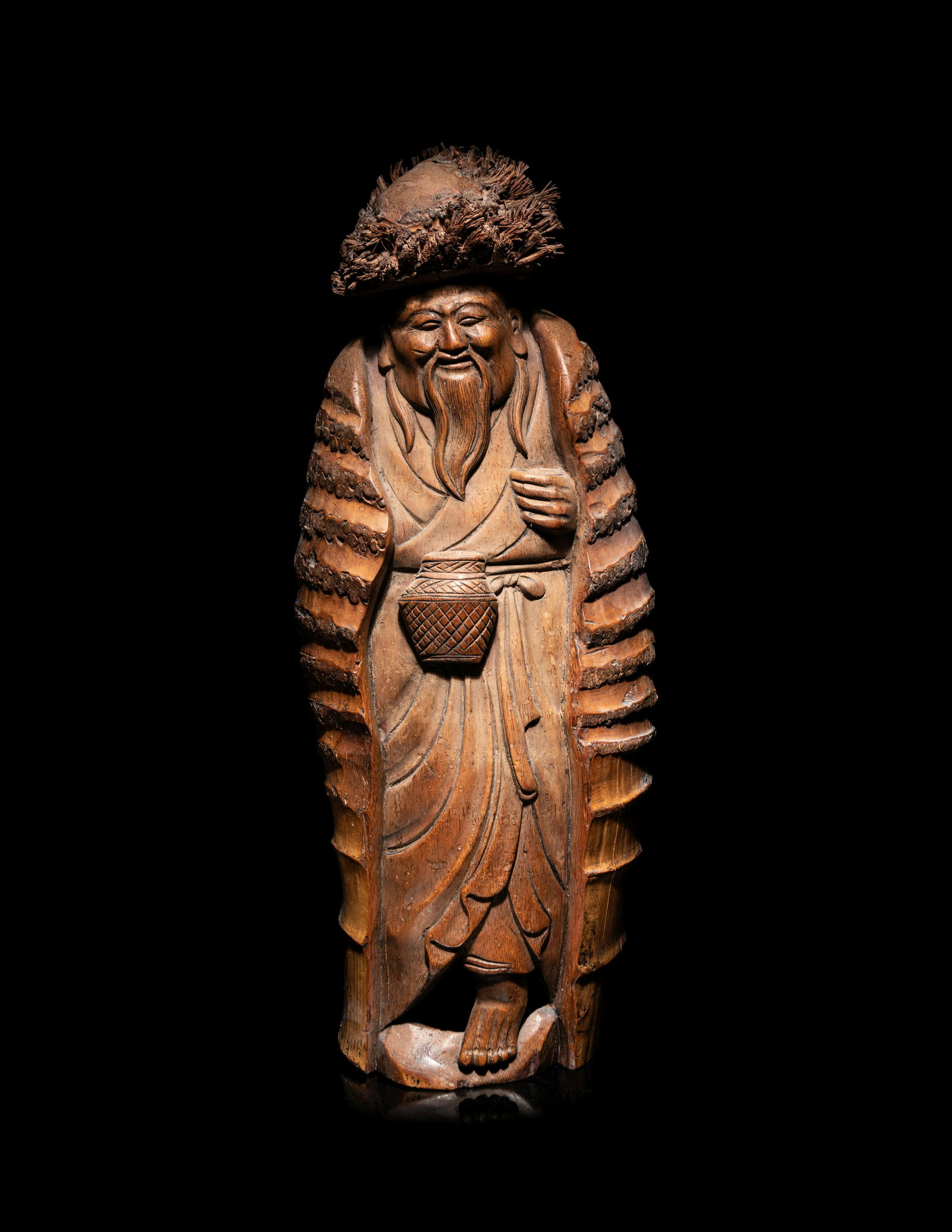 A Japanese Carved Bamboo Figure of an Elderly: A Japanese Carved Bamboo Figure of an Elderly the figure depicted standing, dressed in draped robes and a long coat, carrying a fish basket along his waist, his face carved with a smile and long beard