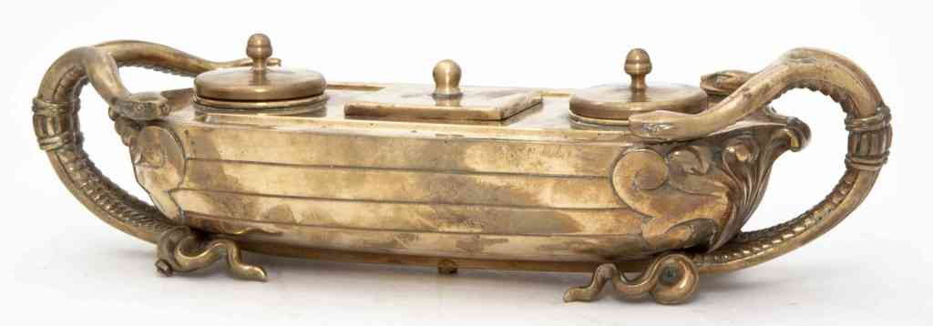 An English Brass Ink Stand, Width 12 inches.: An English Brass Ink Stand, in a classical boat form with acanthus leaf accents, having double handles modeled after two pairs of serpents and stylized serpent's tail feet. Width 12 inches.