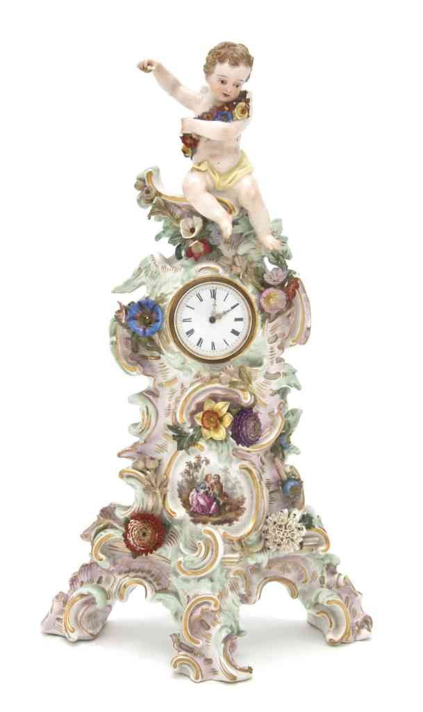 A Meissen Porcelain Figural Clock, Height 11 1/2 i: A Meissen Porcelain Figural Clock, surmounted with a cherub over the foliate and Rococo decorated case, having time only movement, with crossed swords mark in underglaze blue, impressed 103, incised 2