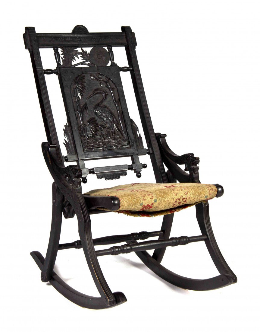 An American Aesthetic Ebonized Rocking Chair, Heig: An American Aesthetic Ebonized Rocking Chair, having a carved splat depicting a crane in a watery landscape, the arms with lion head terminals, with incised decoration throughout. Height 35 1/4 inches