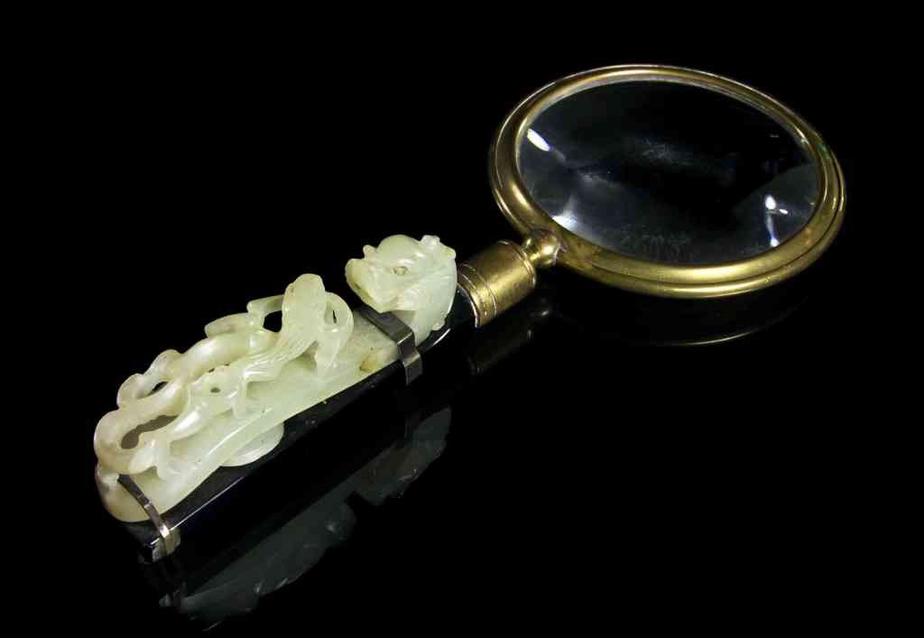 A Jade Garment Hook, Length of hook 3 inches.: A Jade Garment Hook, having a sinuous dragon on the back, mounted as a magnifying glass with brass mount stamped Made in Germany with black glass handle. Length of hook 3 inches. Property from the Est