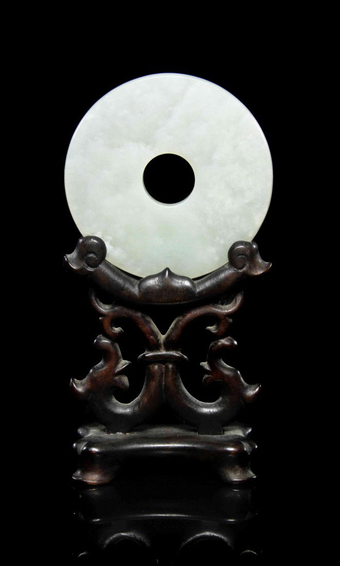 A Jade Bi, Height 2/4 inches.: A Jade Bi, of celadon colored stone, raised upon a wood base. Height 2/4 inches. Property from Ms. Irene Dean, City Department National Committee Y.W.C.A., Shanghai China, August 1924.