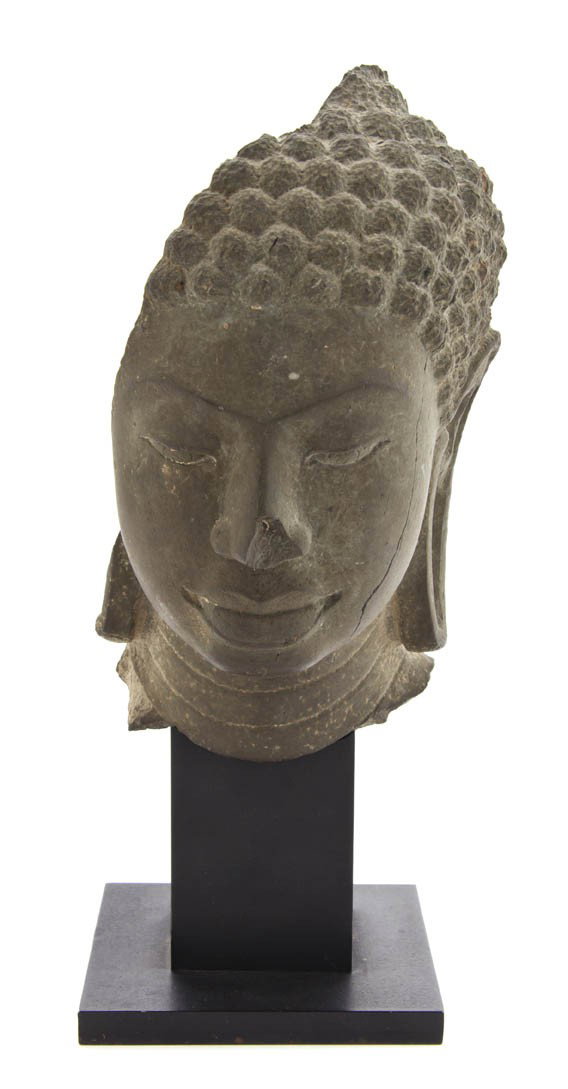 A Southeast Asian Stone Model of the Head of Buddh: A Southeast Asian Stone Model of the Head of Buddha, the gray stone face depicted with a serene expression, having articulated hair knots and elongated ear lobes. Height 10 inches.