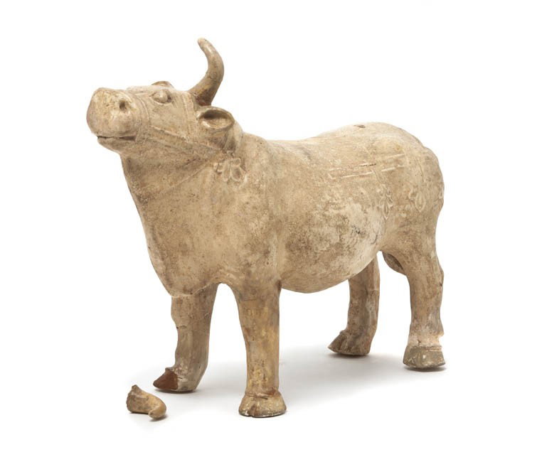 A Pottery Tomb Figure of an Ox, Length 9 1/8 inche: A Pottery Tomb Figure of an Ox, Tang Dynasty, the forward facing animal having raised decoration of riggings with straw glaze throughout. Length 9 1/8 inches.