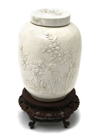 A White Ginger Jar and Lid, Height of jar 10 1/2 i: A White Ginger Jar and Lid, having raised flower decoration, with wood stand. Height of jar 10 1/2 inches.
