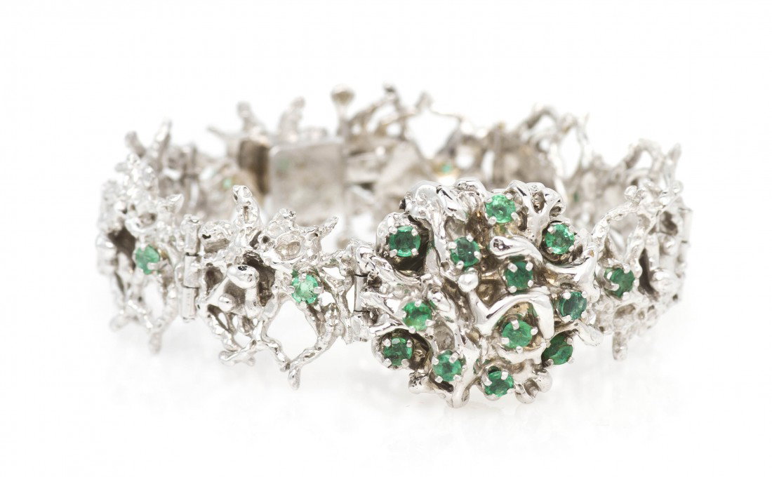 A 14 Karat White Gold and Emerald Wristwatch, 33.0: A 14 Karat White Gold and Emerald Wristwatch, with hinged surprise dial cover, containing numerous round brilliant cut emeralds, silvered dial, Arabic numerals, black baton hands, snap on case back, m