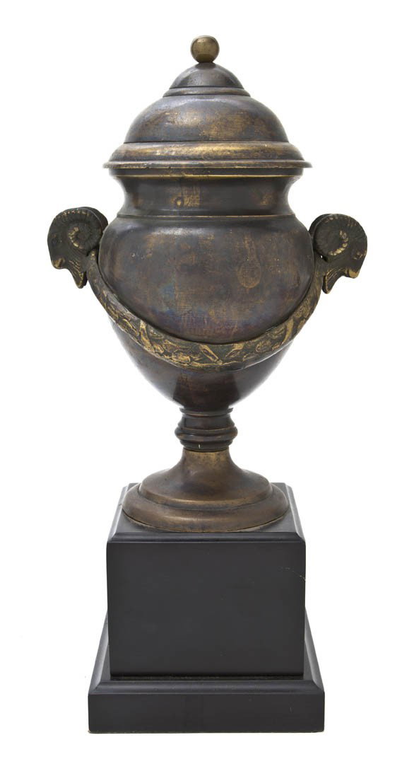A Continental Bronzed Metal Covered Urn, Height o: A Continental Bronzed Metal Covered Urn, the baluster body with ram mask handles and foliate swag decoration, mounted on an ebonized wood plinth. Height overall 14 inches.