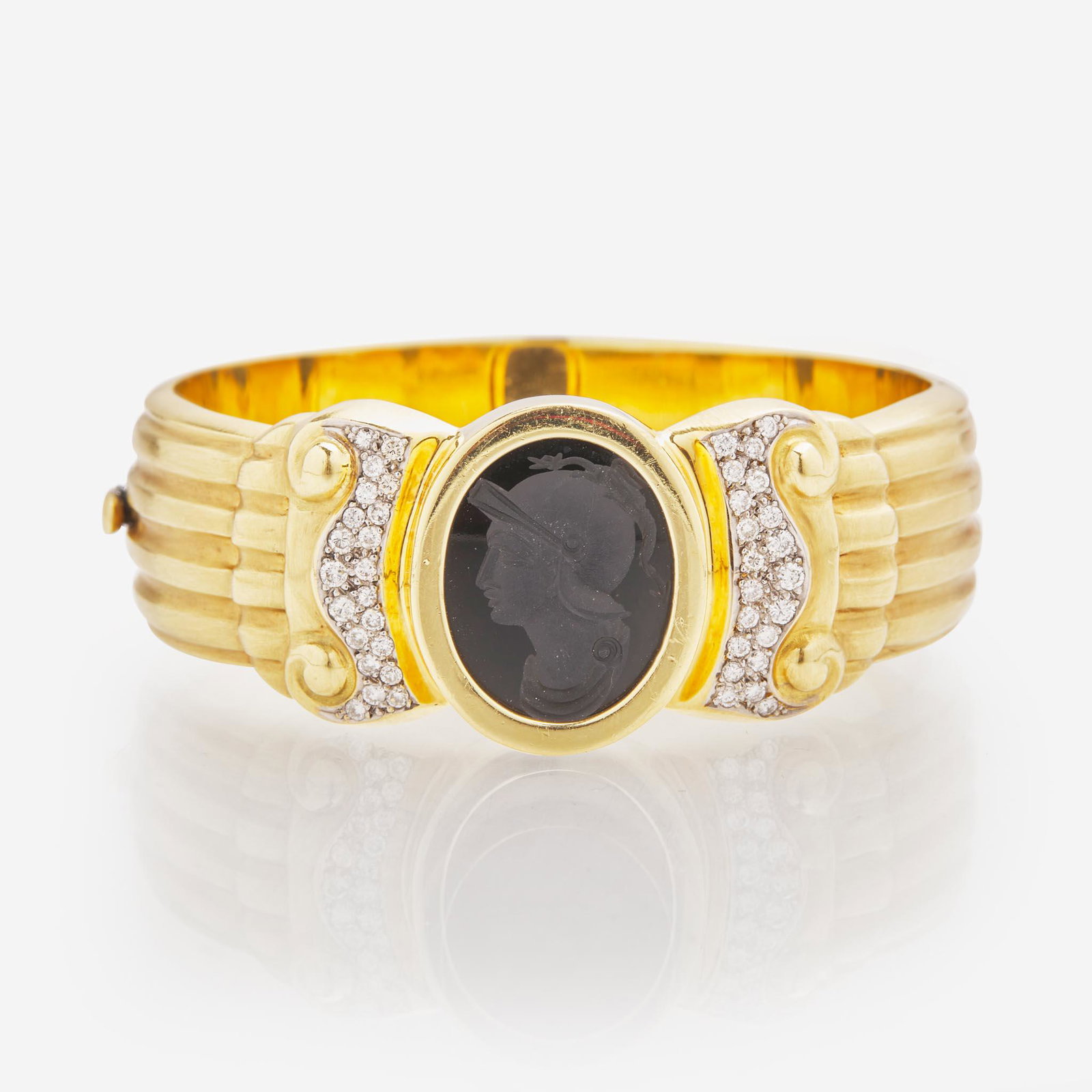 An 18K Yellow Gold Intaglio Bangle: An 18K Yellow Gold Intaglio Bangle An 18K yellow gold textured bangle centering a bezel-set black onyx intaglio cameo and accented by forty-two round brilliant-cut diamonds. Diamonds are near colorles