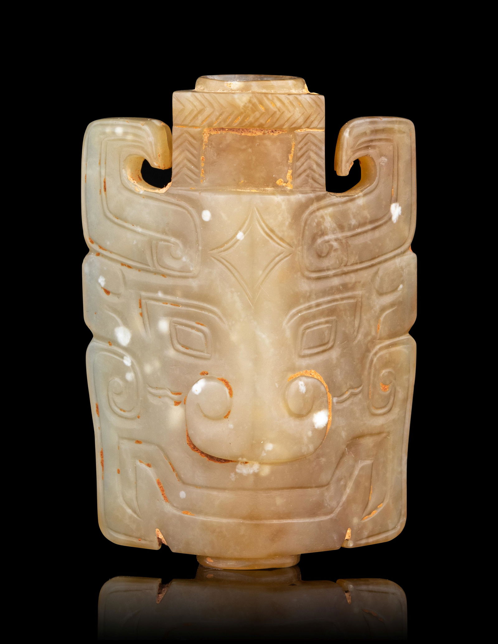 A Small Archaistic Jade Mask-Form Ornament: A Small Archaistic Jade Mask-Form Ornament 黃玉仿古牌 the front carved with a pair of lozenge-shaped eyes above a nose formed by two c-scrolls and a wide mouth, the stone