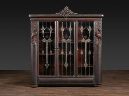 An Aesthetic Movement Crane and Mask Carved Mahogany and Glass Paneled Bookcase: An Aesthetic Movement Crane and Mask Carved Mahogany and Glass Paneled Bookcase Attributed to the workshop of Alexander Roux, New York, Late 19th Century Height 81 x width 73 x depth 15 1/2 inches.