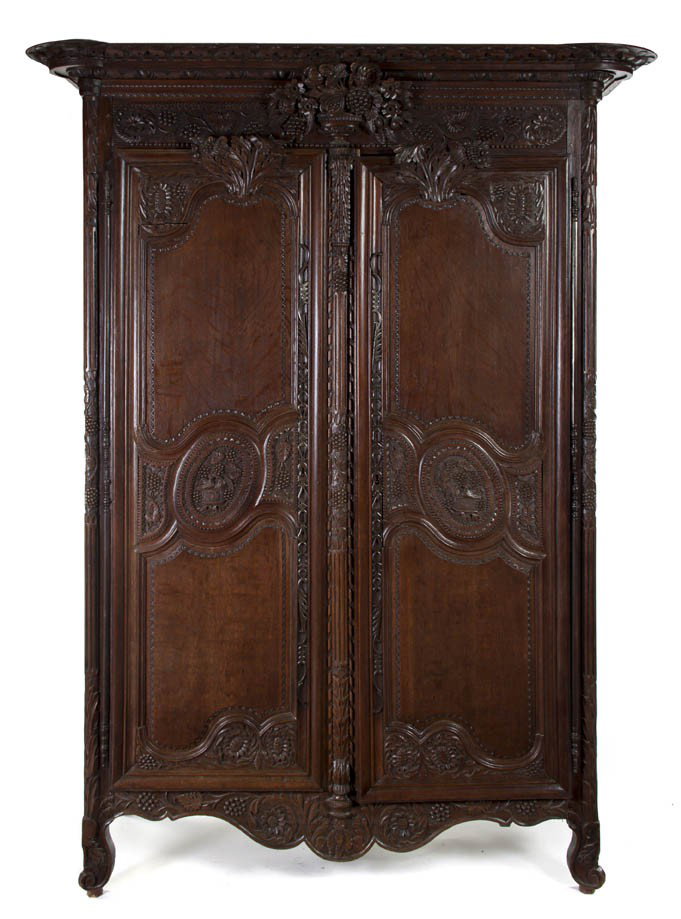 A Brittany Carved Armoire, Height 97 1/4 x width 7: A Brittany Carved Armoire, 18th century and later, having a flaring cornice with turret corners over the frieze centered with a fruit and floral basket, the case with two doors carved throughout, rais