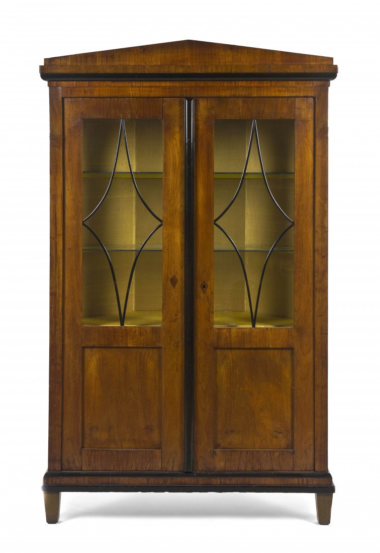 A Biedermeier Corner Cabinet, Height 74 x width 43: A Biedermeier Corner Cabinet, having a peaked crest over two glazed and paneled doors with ebonized mullion, raised on block feet. Height 74 x width 43 1/2 x depth 25 inches. Property from the Estate 