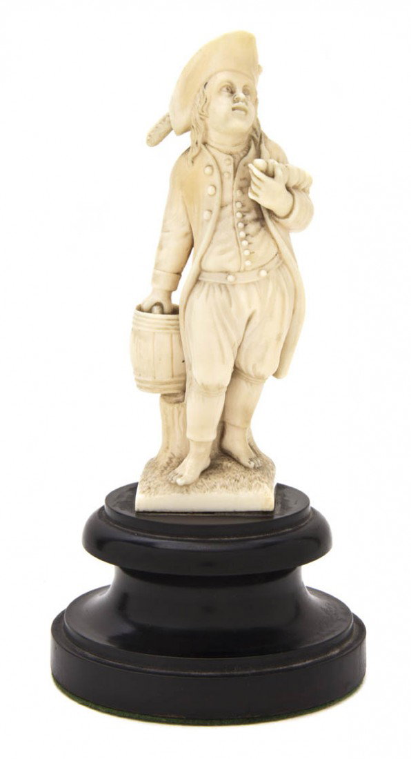 A Continental Carved Ivory Figure, Height of ivory: A Continental Carved Ivory Figure, 18th/19th century, depicting a barefoot gentleman in a tri-corner hat holding a pail, raised on an ebonized wood pedestal base. Height of ivory 4 3/8 inches.