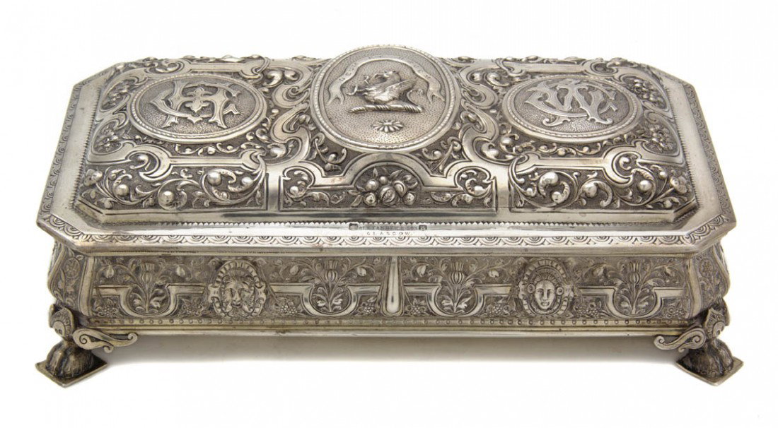 A Scottish Silver Box, Alexander & Son, Width 8 1/: A Scottish Silver Box, Alexander & Son, Glasgow, 1881, the hinged lid centered with a family crest of a griffin flanked by raised monograms over a decorated frieze having thistles and masks, raised on
