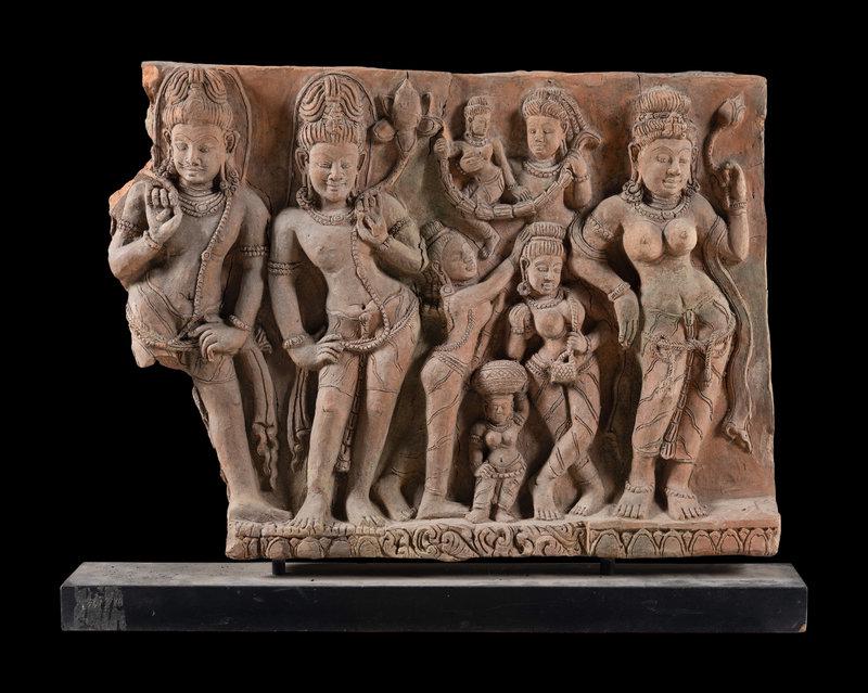 A Large Indian Carved Sandstone Relief Panel: A Large Indian Carved Sandstone Relief Panel depicting three standing figures, each holding a lotus sprig in the hand, and six smaller figures in the center. Height without stand 22 1/4 in., 56.5 cm.<