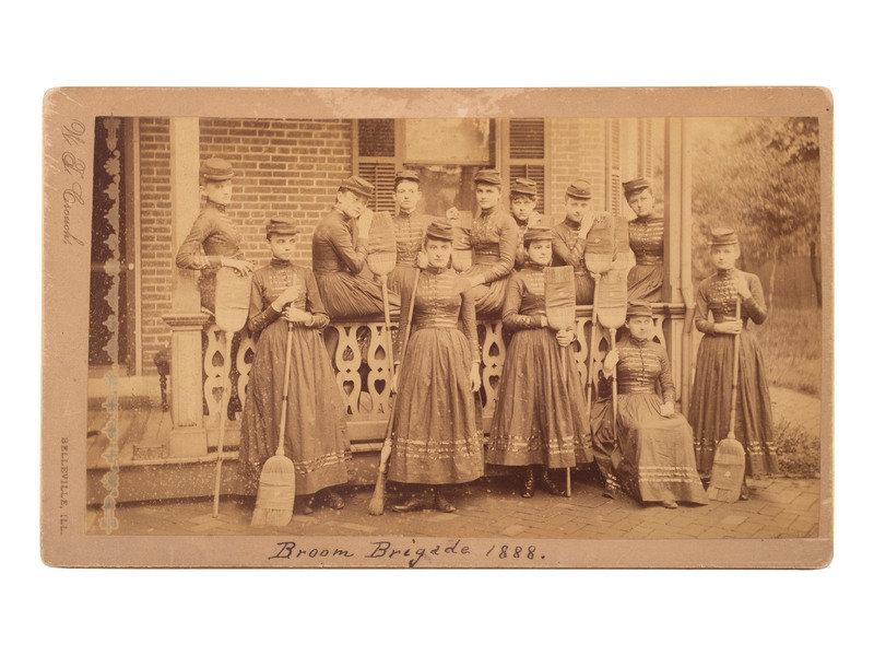 [WOMEN]. Broom Brigade 1888. Boudoir photograph of an all-female military-style drill team.: [WOMEN]. Broom Brigade 1888. Boudoir photograph of an all-female military-style drill team. 7 3/4 x 4 1/2 in. albumen photograph on cardstock mount (light toning, significant spotting, wear to mount e