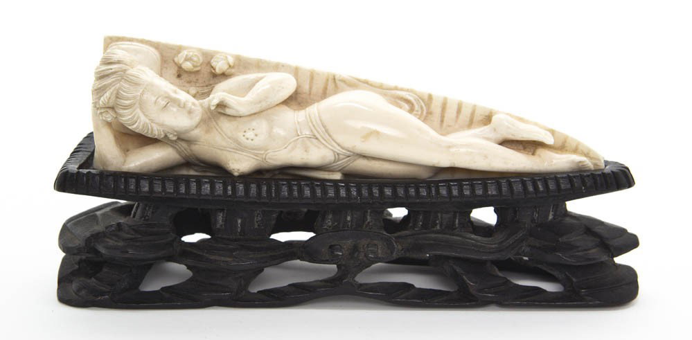 A Chinese Ivory Doctor's Model, Length of ivory 6: A Chinese Ivory Doctor's Model, the figure depicted with a coiffeur and earrings, reclining by a folding fan and flowers on a tapering grooved base, set upon a carved and ebonized wood stand. Length o
