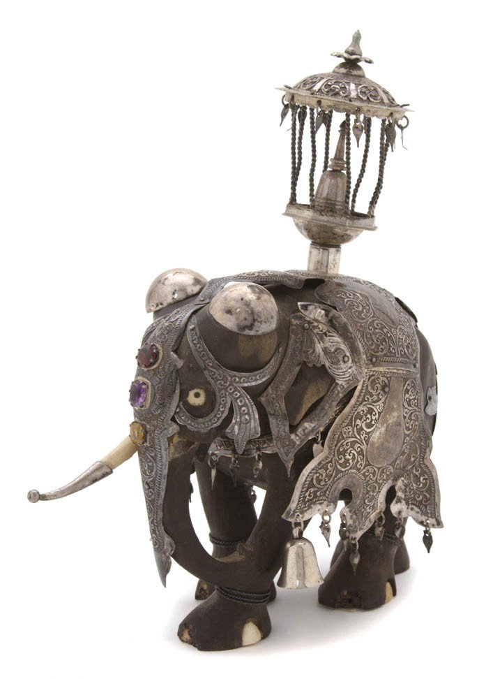 An Indian Carved Wood and Silver Mounted Elephant: An Indian Carved Wood and Silver Mounted Elephant, the animal having tooled metal decoration throughout the saddle blanket and mounts, having three colored stones mounted on the forehead, with a cover