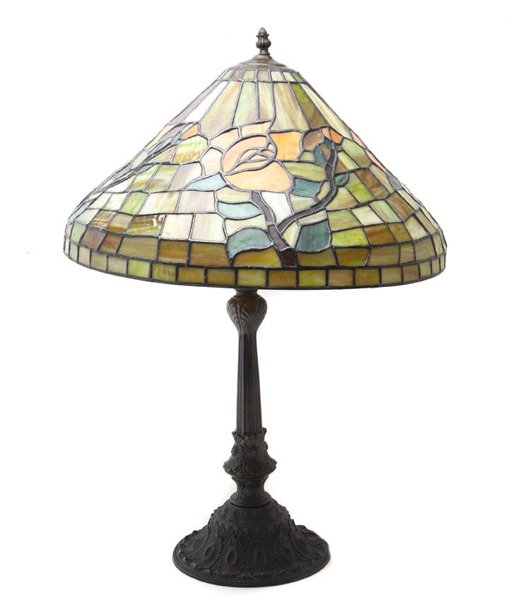 An American Leaded Glass Table Lamp, Height overa: An American Leaded Glass Table Lamp, the conical shade decorated with roses among mottled geometric tiles, raised on a floral cast base. Height overall 30 1/8 inches; diameter of shade 21 inches.