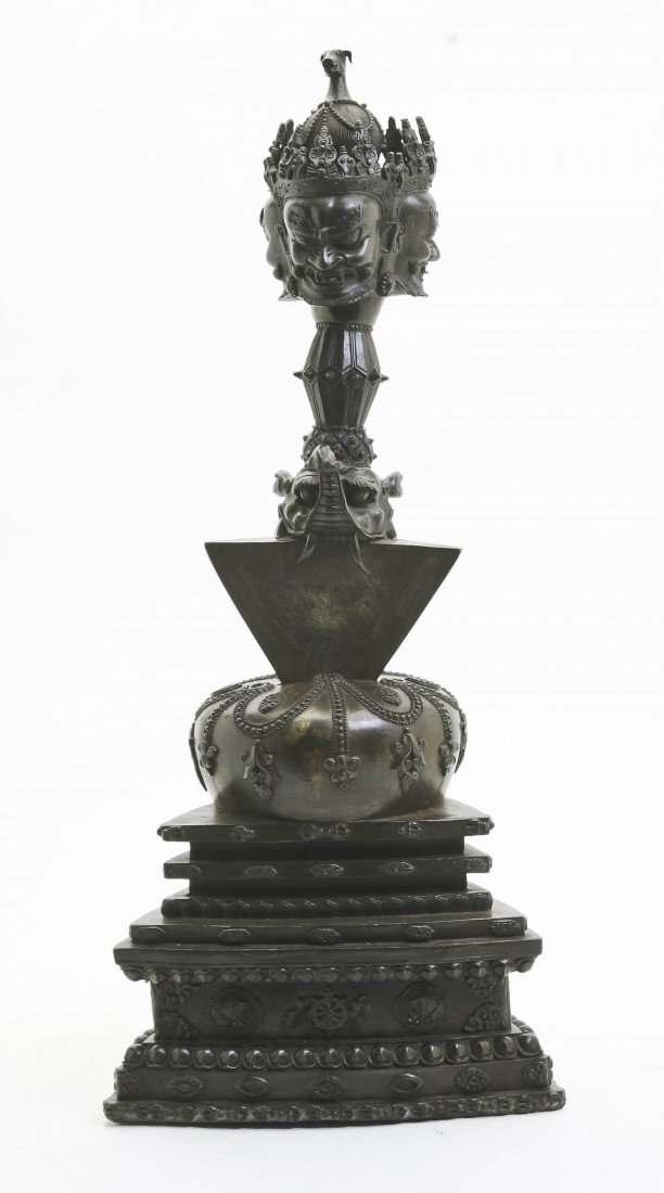 A Nepalese Patinated Bronze Statue, Height overal: A Nepalese Patinated Bronze Statue, in two parts, the top decorated with three masks above a beast, raised on a stepped base with allover scrolling decoration. Height overall 20 1/2 inches.