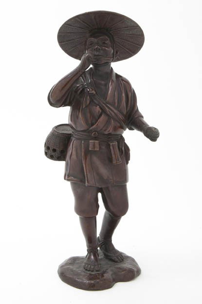 A Japanese Bronze Figure of a Man, Height 11 5/8: A Japanese Bronze Figure of a Man, depicted wearing a straw hat, short robe and sandals, with a woven basket and netsuke tied around his waist, set on a naturalistic base with a three character maker'