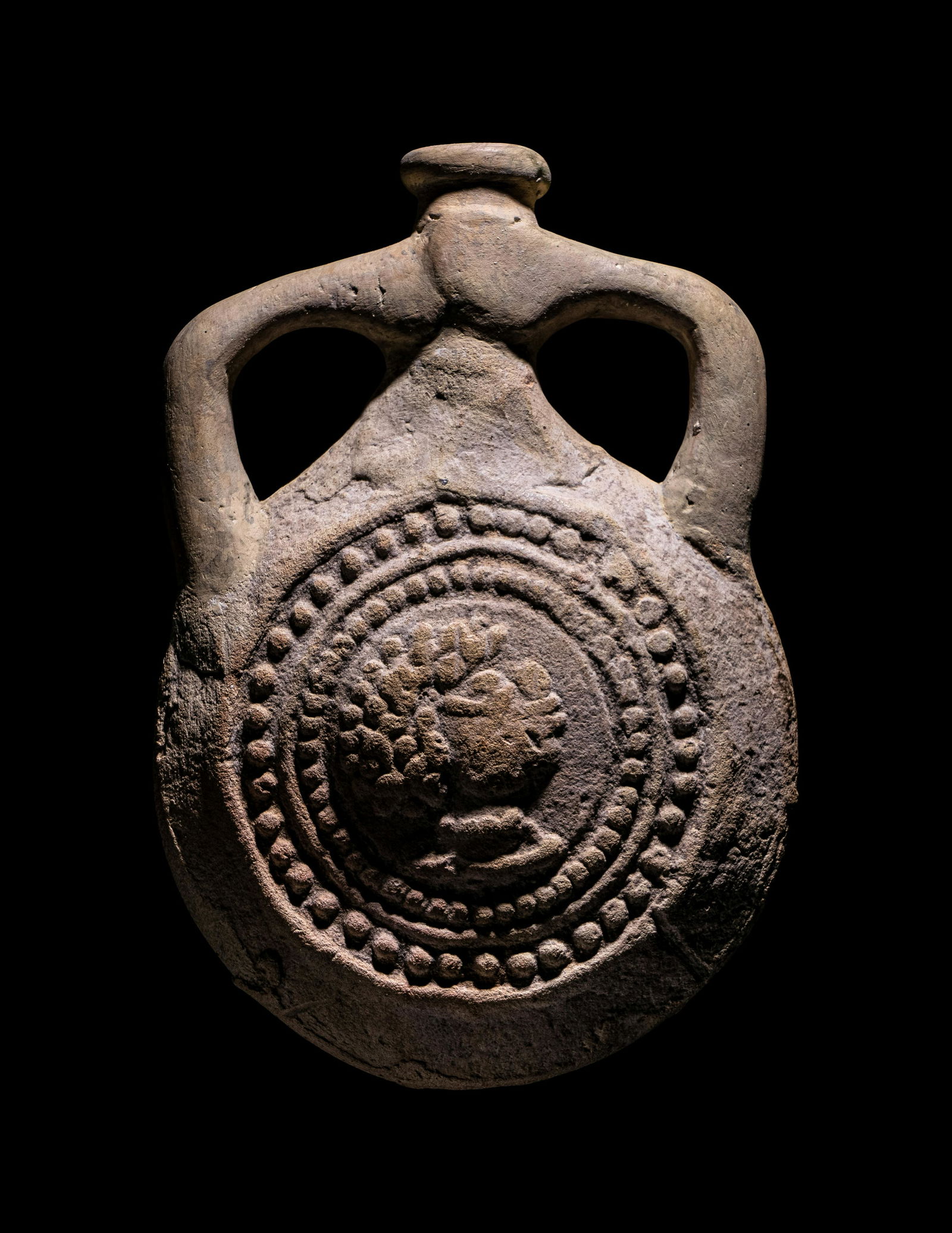 A Coptic Terracotta Pilgrim Flask with Saint Menas and Inscription: A Coptic Terracotta Pilgrim Flask with Saint Menas and Inscription Circa 400-600 A.D. Height 4 inches (10.2 cm). Property from the Harer Family Trust Collection Provenance: Acquired from Fagan Arms, C