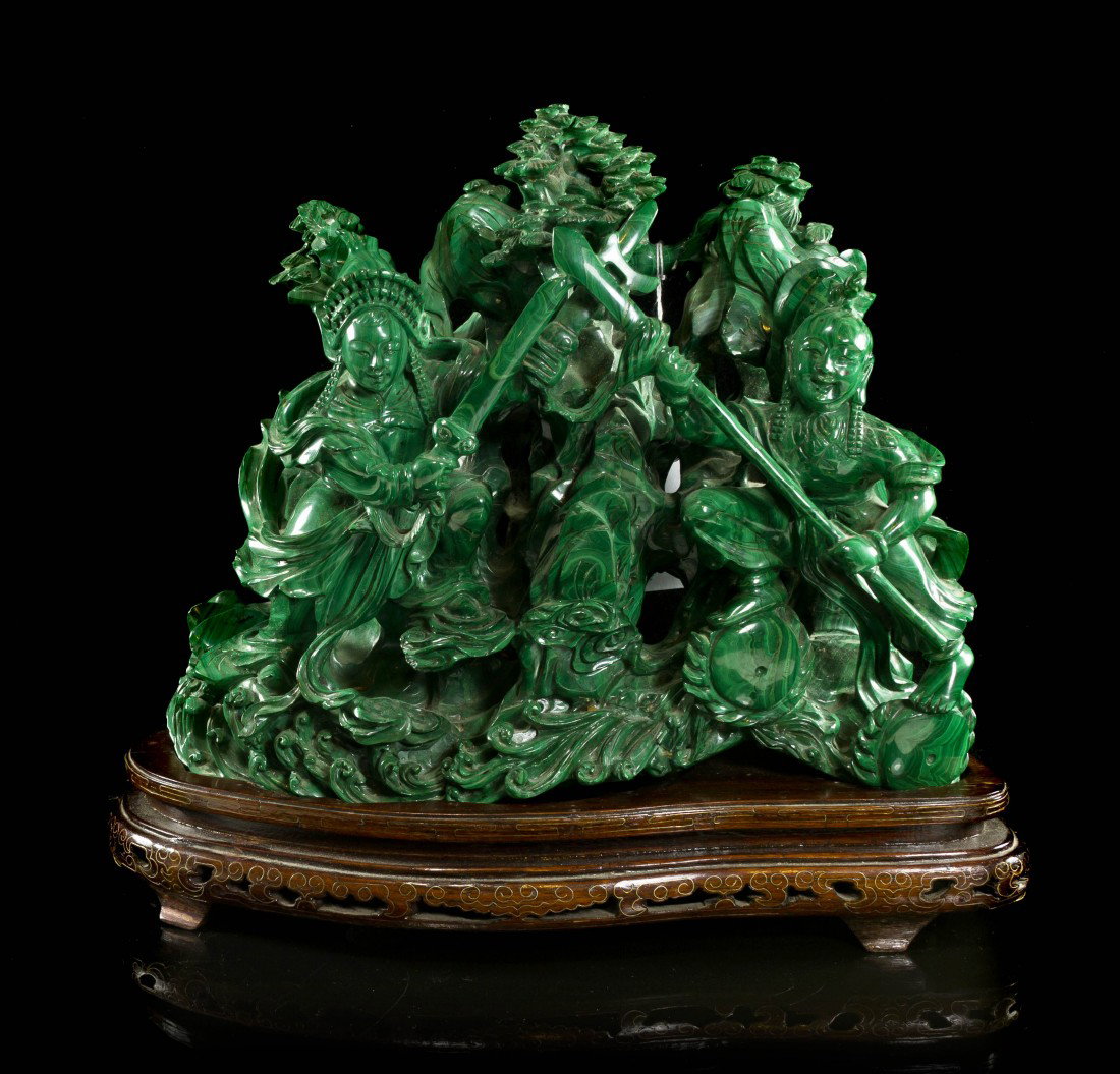 A Large Malachite Figural Carving, Height 9 1/8 x : A Large Malachite Figural Carving, depicting two warriors at the front with crossed weapons, having rock forms throughout issuing pine trees, with a wave form base and raised atop a fitted hardwood ba